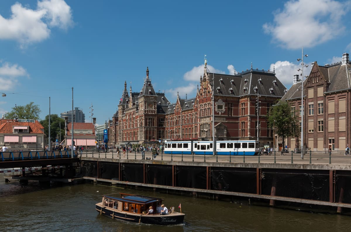 The red-brick facade of Amsterdam Centraal station under a blue sky