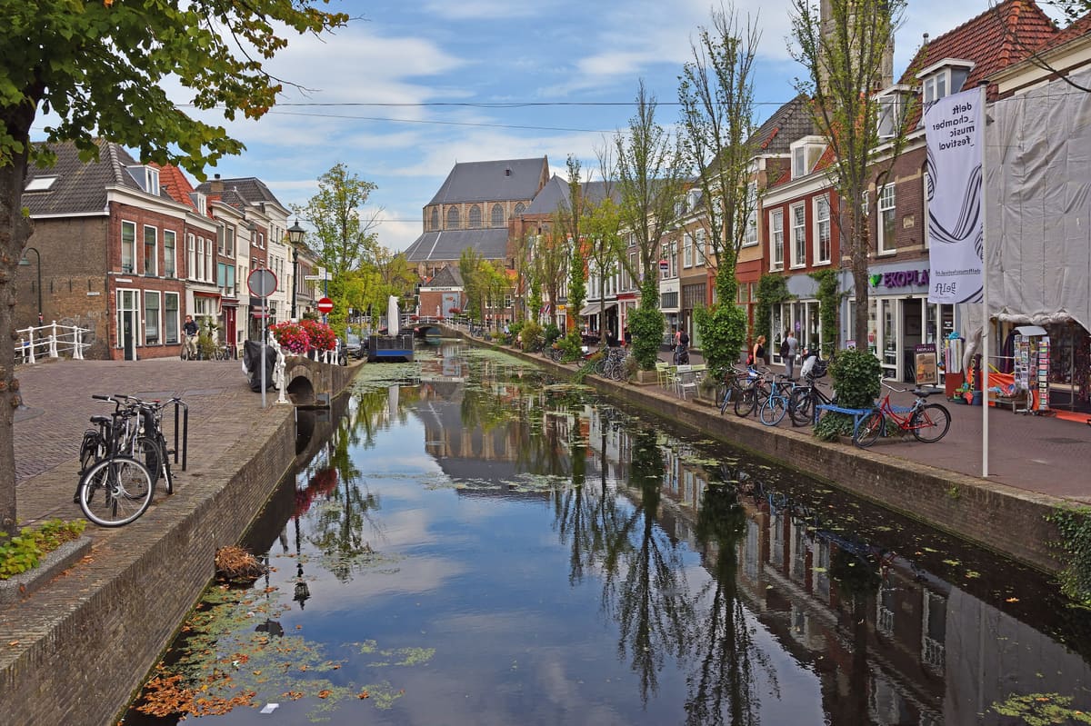 A tree-lined canal in the centre of Delft with brick houses and the Nieuwe Kerk tower behind